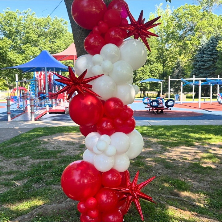 Red and white spiral balloon garland outdoors at a park